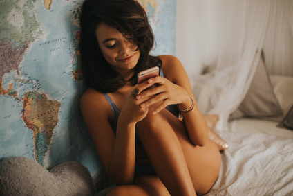 Portrait of sexy afro-american woman uses smartphone in bedroom